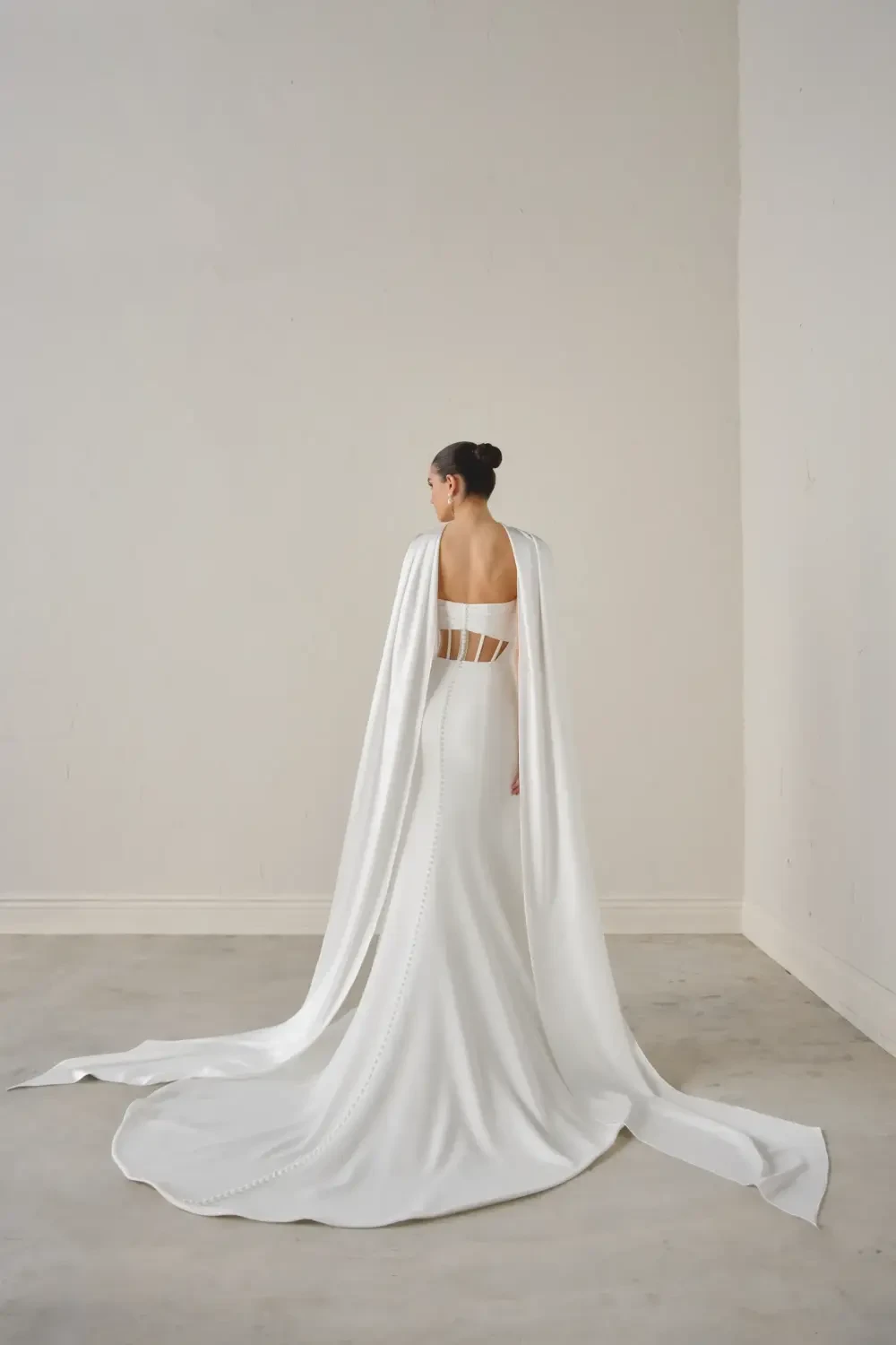 A model wearing a sleek white strapless gown with a draped scarf around the neck, posing against a neutral background.